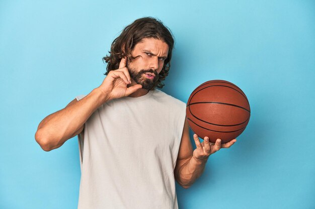 Uomo barbuto con il basket in studio blu che cerca di ascoltare un pettegolezzo