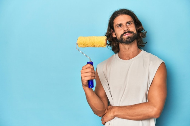 Uomo barbuto con un rullo di vernice in un ambiente di studio blu