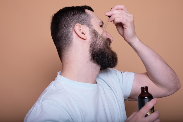 Uomo barbuto con una pipetta con olio di barba su sfondo beige