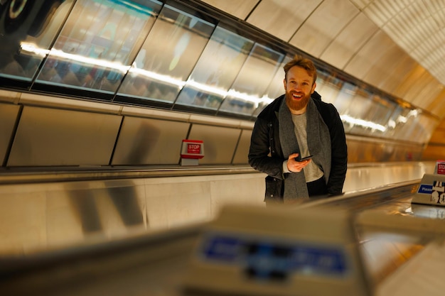 Uomo barbuto con uno smartphone su una scala mobile nella metropolitana