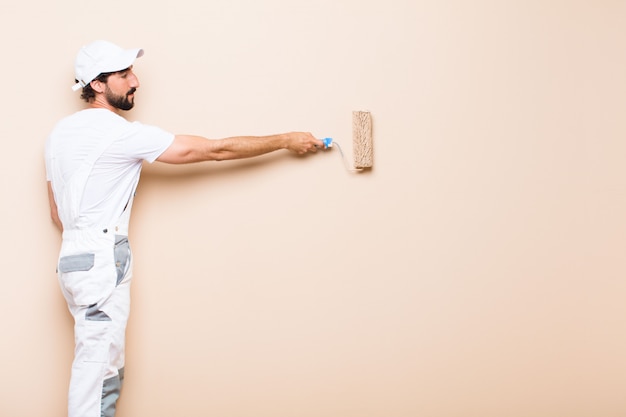 Uomo barbuto del giovane pittore che vernicia un muro con un rullo di vernice