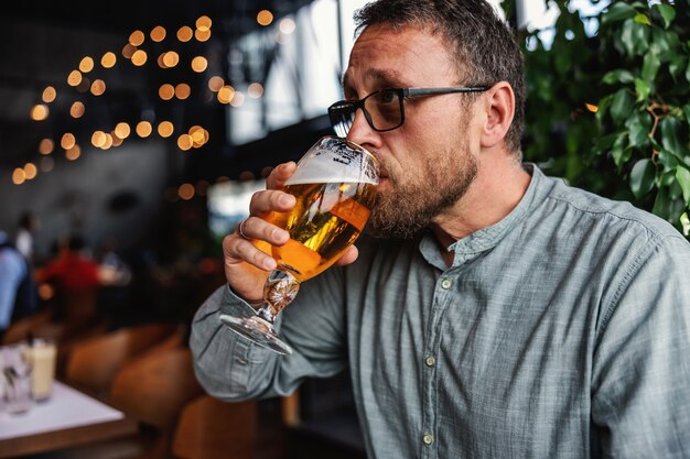 Uomo barbuto di mezza età seduto in un bar e bere birra chiara fredda fresca. È ora di rilassarsi dopo il lavoro. Avere sempre un po 'di tempo per te stesso.