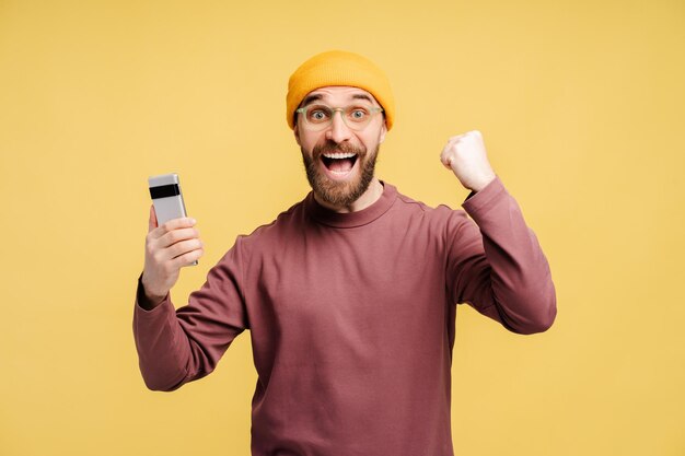 Uomo barbuto emotivo che urla di gioia e si sente sopraffatto di gioia mentre tiene in mano lo smartphone