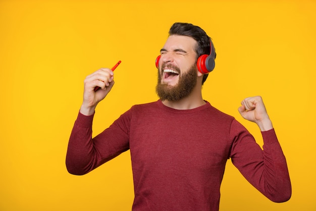 Uomo barbuto emozionante, godendo la sua canzone preferita con le nuove cuffie, ballando su sfondo giallo