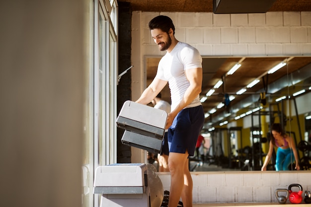 Uomo barbuto felice allegro muscolare forte smistamento stepper in palestra vicino alla finestra e allo specchio.