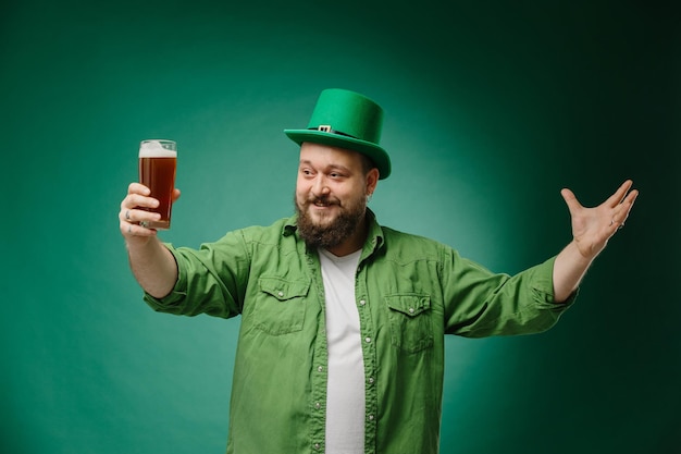 Uomo barbuto felice con un bicchiere di birra su uno sfondo verde scuro Celebrazione del giorno di San Patrizio