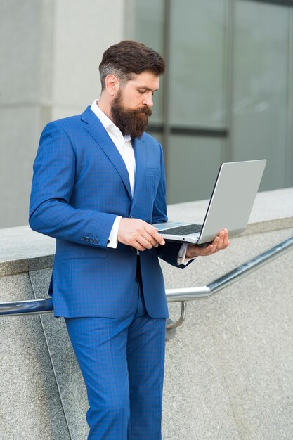 Uomo barbuto in abito formale controlla la posta elettronica nel laptop utilizzando l'e-mail all'aperto urbano di Internet