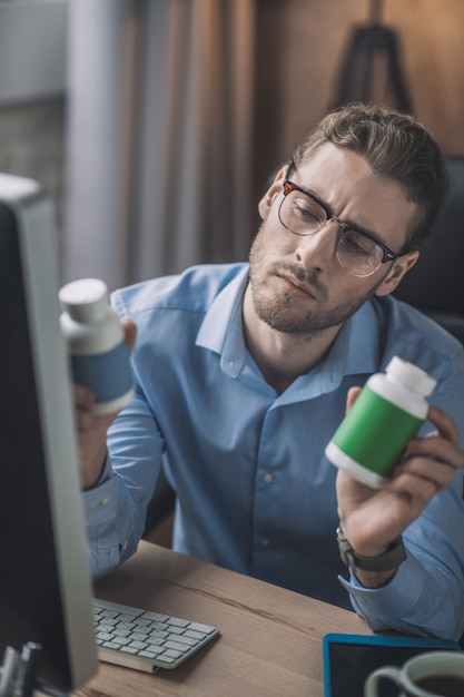 Uomo barbuto in camicia blu che legge sulle vitamine