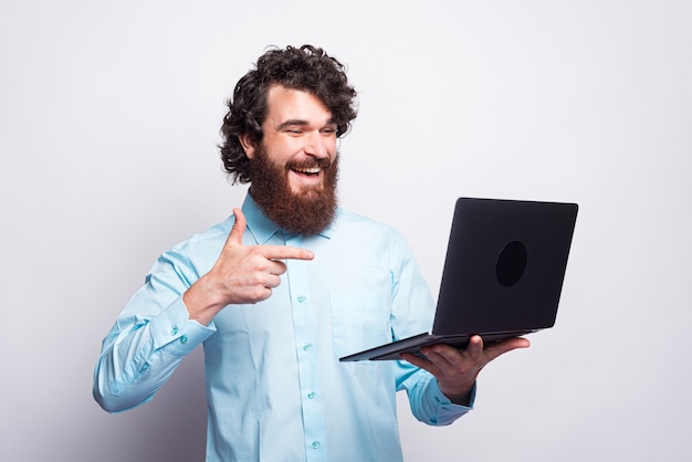 Uomo barbuto in casual che punta al computer portatile e sorridente