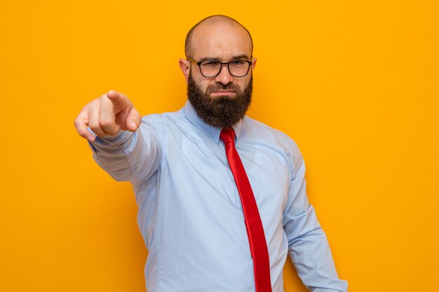 Uomo barbuto in cravatta rossa e camicia blu con gli occhiali che guarda con una faccia seria che punta con il dito indice davanti