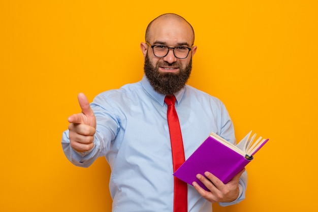 Uomo barbuto in cravatta rossa e camicia blu con gli occhiali con in mano un libro che punta con il dito indice davanti