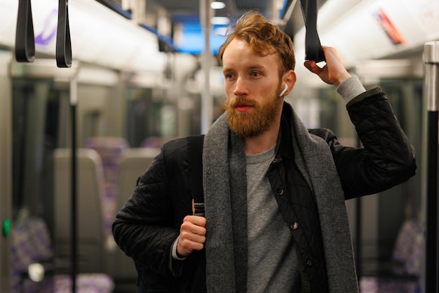 Uomo barbuto in cuffie wireless e con uno zaino è in piedi in un treno della metropolitana