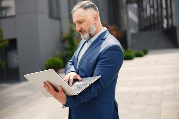 Uomo barbuto in piedi e utilizzando un computer portatile davanti all'ufficio moderno