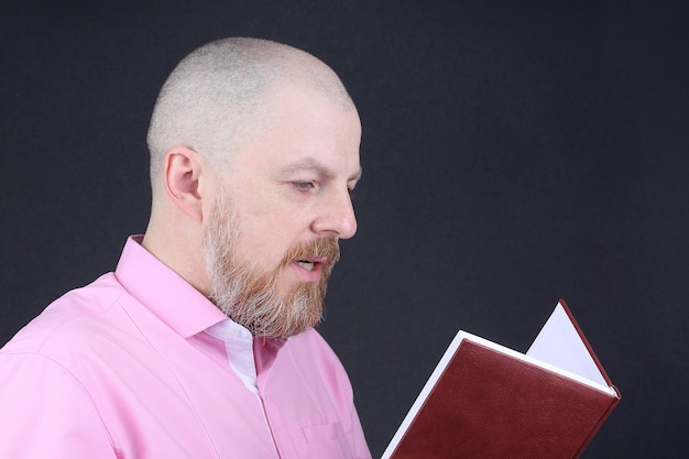 Uomo barbuto in una camicia rosa che legge un libro