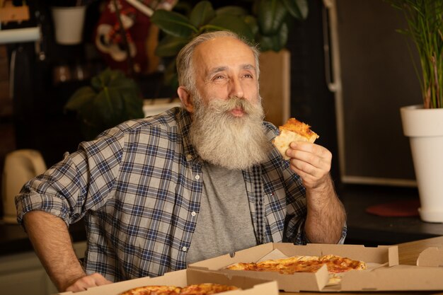 Uomo Barbuto in una cucina. Un uomo anziano in una camicia blu. Maschio a casa con la pizza.