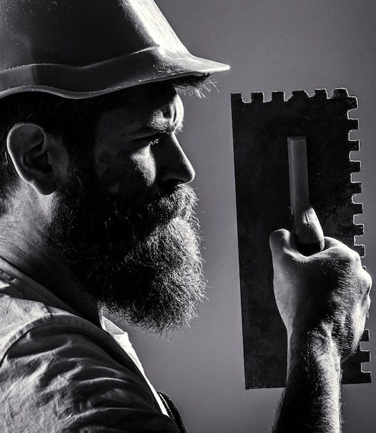 Uomo barbuto lavoratore barba costruzione casco elmetto strumenti di intonacatura strumento cazzuola tuttofare uomo costruttore muratore strumenti costruttore costruttori in elmetto casco bianco e nero