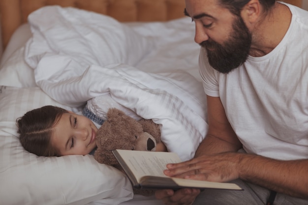 Uomo barbuto maturo che riposa a casa con la sua piccola figlia