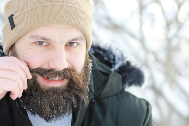 Uomo barbuto nei boschi d'inverno. Il giovane felice attraente con la barba cammina nel parco.