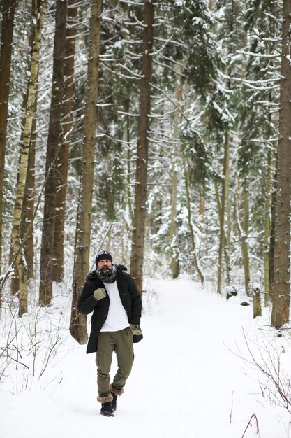 Uomo barbuto nei boschi invernali. Attraente giovane felice con la barba a piedi nel parco.