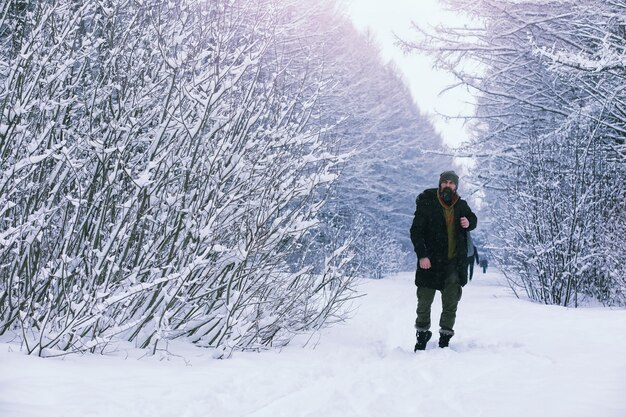 Uomo barbuto nei boschi invernali. Attraente giovane felice con la barba a piedi nel parco.