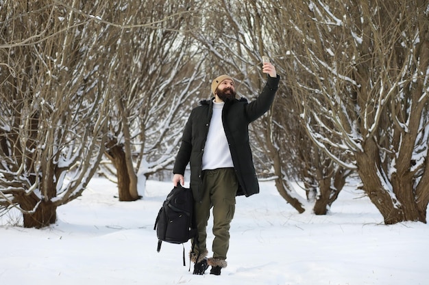 Uomo barbuto nei boschi invernali. Attraente giovane felice con la barba a piedi nel parco.