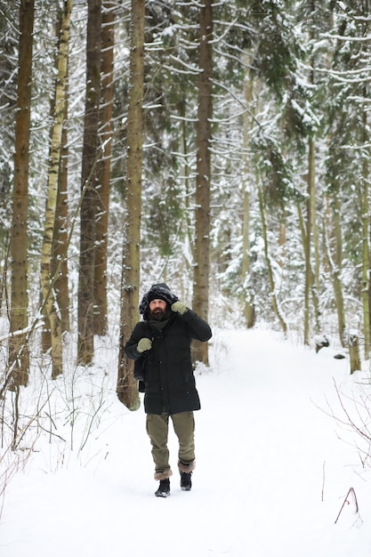 Uomo barbuto nei boschi invernali. Attraente giovane felice con la barba a piedi nel parco.