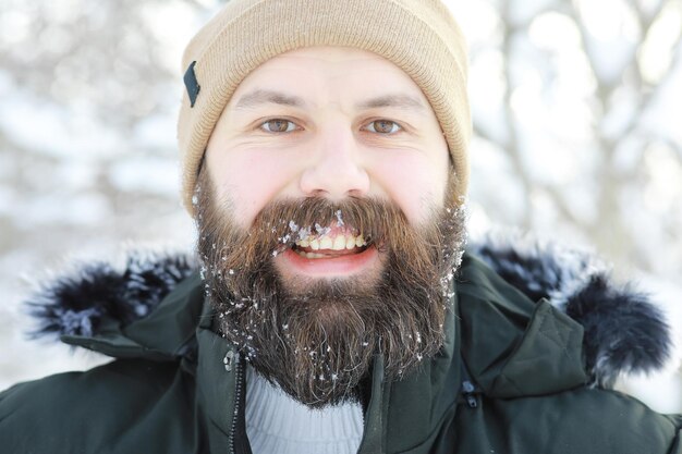 Uomo barbuto nei boschi invernali. Attraente giovane felice con la barba a piedi nel parco.