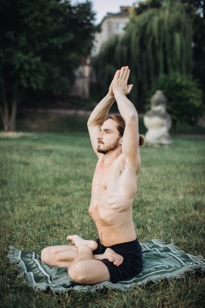 Uomo barbuto nella posa del loto che si siede sull'erba verde, concetto di calma e meditazione,