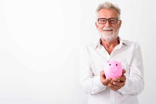 uomo barbuto senior felice che sorride mentre tiene il salvadanaio con gli occhiali su bianco