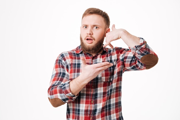 Uomo barbuto sorpreso in camicia che mostra il segno del telefono