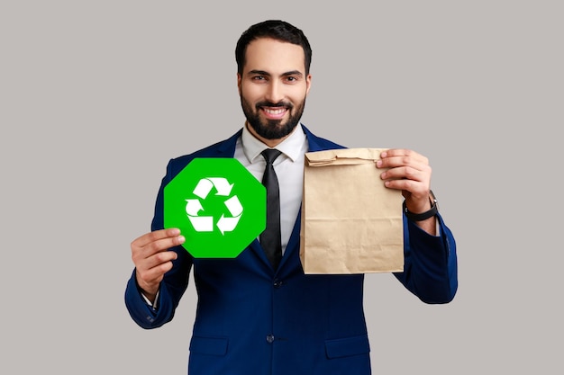 Uomo barbuto sorridente che tiene in mano un cartello di riciclaggio verde e un pacchetto di carta che pensa in verde