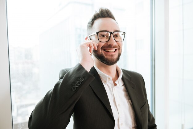 Uomo barbuto sorridente di affari che parla sul telefono