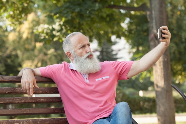 Uomo barbuto su una panchina prendendo un selfie