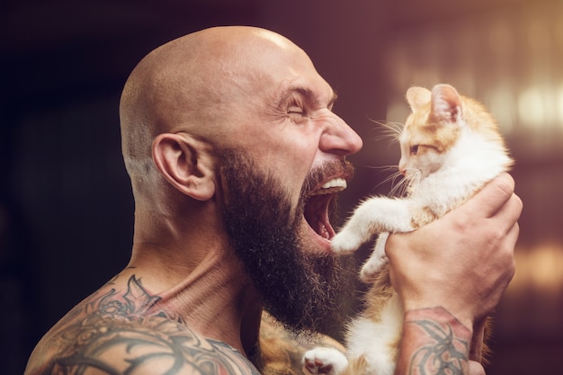 Uomo barbuto tatuato brutale con gatto in palestra