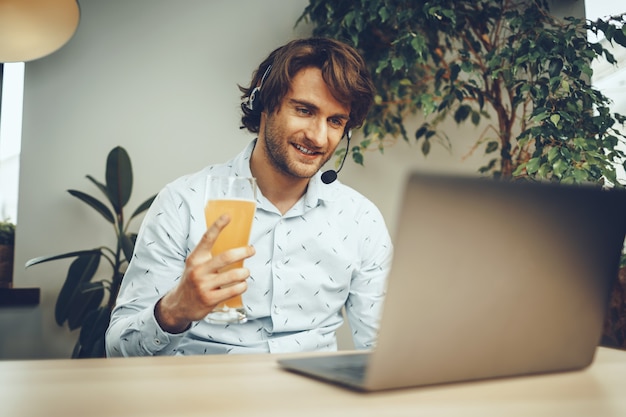 Uomo Barbuto usando il suo laptop mentre beve un bicchiere di birra