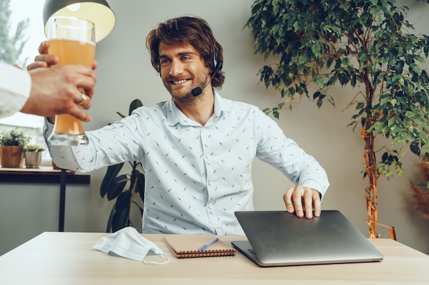 Uomo Barbuto usando il suo laptop mentre beve un bicchiere di birra