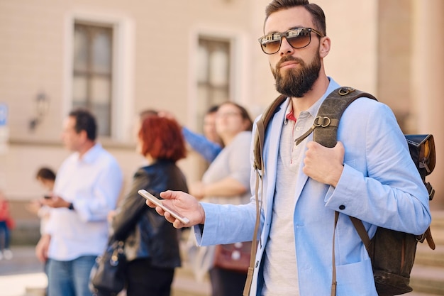 Uomo barbuto viaggiatore urbano con uno zaino tramite smartphone.