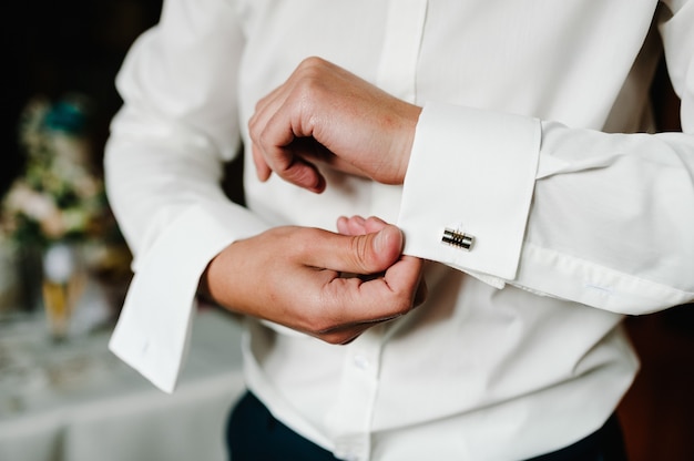 Uomo bello abbottonatura gemelli sulla camicia bianca. Elegante gemello da uomo in oro da sposo. preparazione del matrimonio mattina dello sposo.