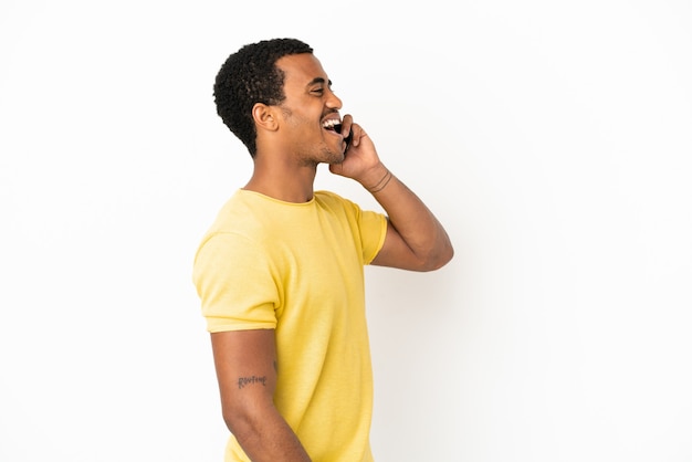Uomo bello afroamericano che utilizza il telefono cellulare sopra fondo bianco isolato che ride nella posizione laterale