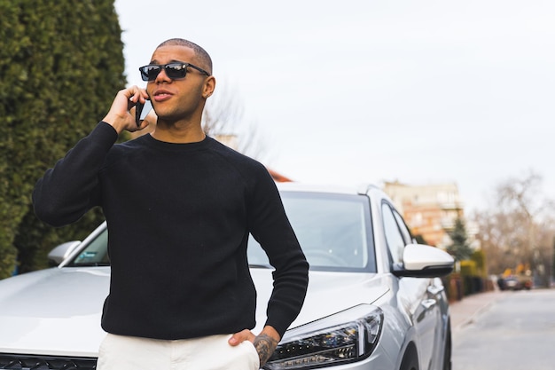 Uomo bello afroamericano felicissimo che parla su un telefono cellulare davanti a un colpo medio dell'automobile