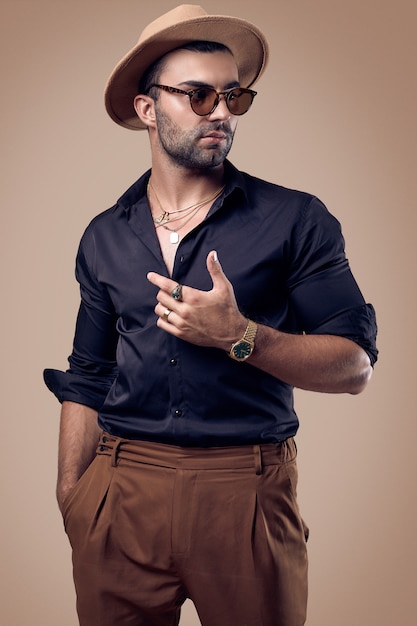 Uomo bello brutale abbronzato hipster in camicia nera, cappello e occhiali