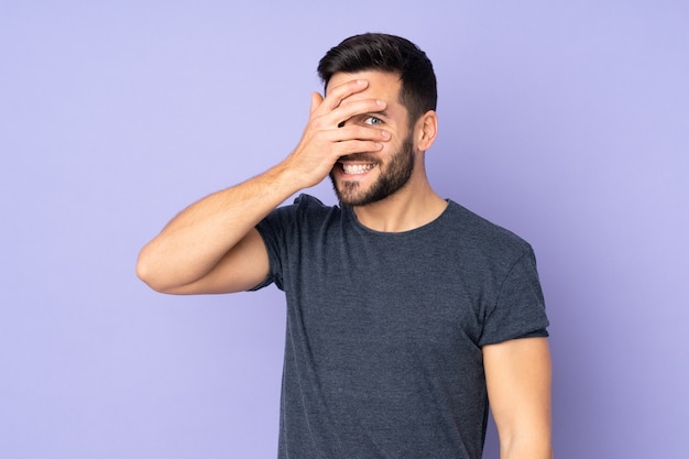 Uomo bello caucasico che copre gli occhi con le mani e sorridente isolato