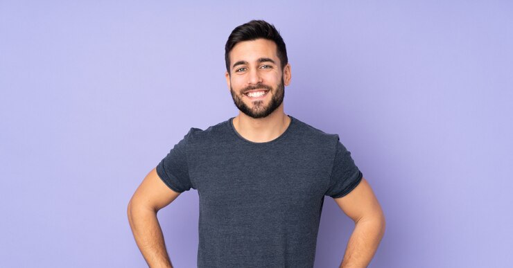 Foto uomo bello caucasico che posa con le braccia all'anca e sorride su un muro viola isolato
