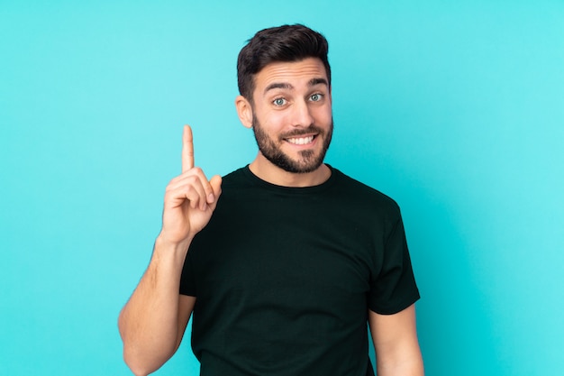 Uomo bello caucasico isolato sulla parete blu che indica con il dito indice una grande idea