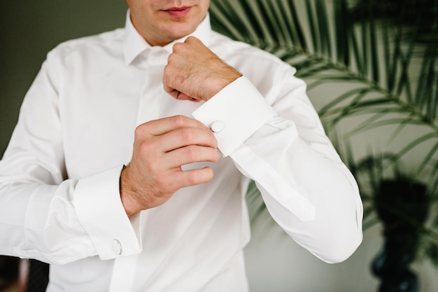 Uomo bello che abbottona i gemelli sulla camicia bianca Sposi elegante maschio oro gemello preparazione del matrimonio mattina dello sposo