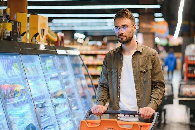 Uomo bello che compra cibo e bevande salutari in un supermercato o in un negozio di alimentari moderno