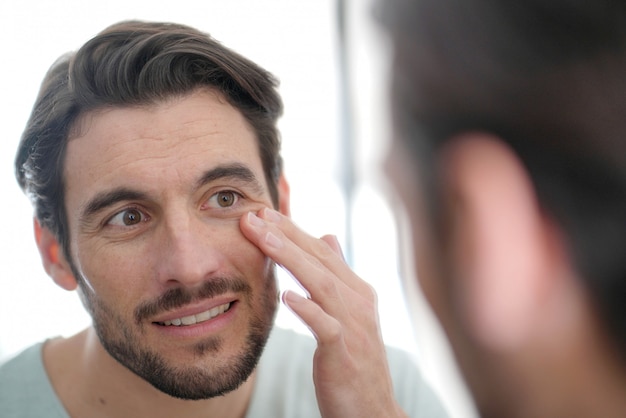 Uomo bello che controlla le grinze in specchio a casa