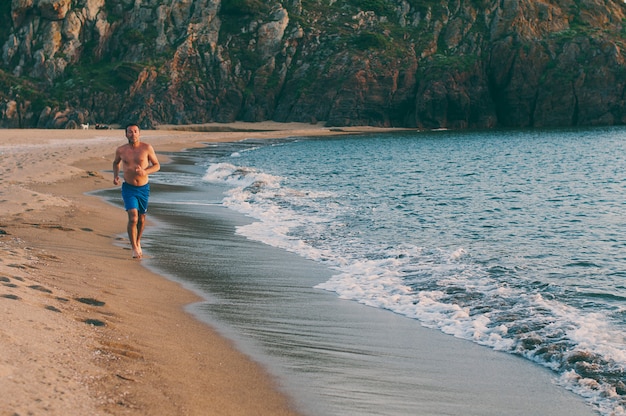 Uomo bello che corre sulla spiaggia al tramonto