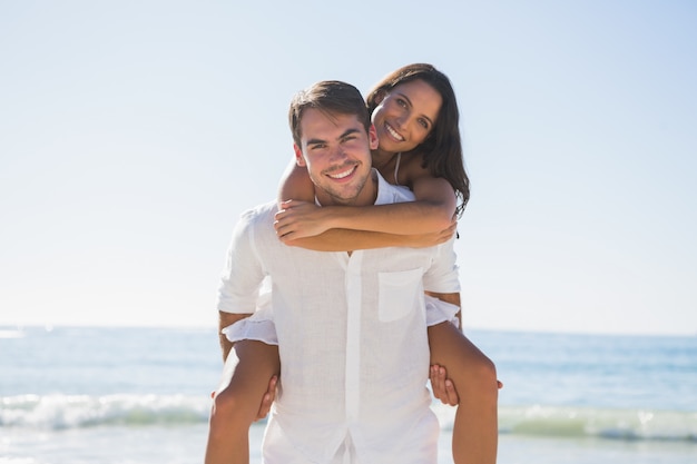 Uomo bello che dà a ragazza un a tre vie che sorride alla macchina fotografica alla spiaggia