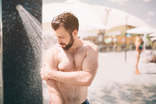 Uomo bello che fa una doccia sulla spiaggia